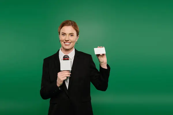 The confident presenter engages viewers, showcasing a blank card, set against a striking green backdrop. — Stock Photo