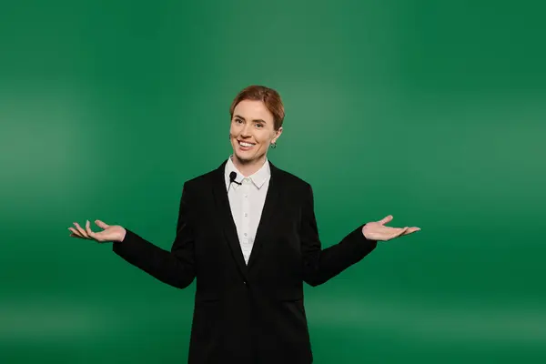 Un presentador de televisión confiado en negro elegante habla con entusiasmo a la audiencia con un fondo verde vivo. - foto de stock