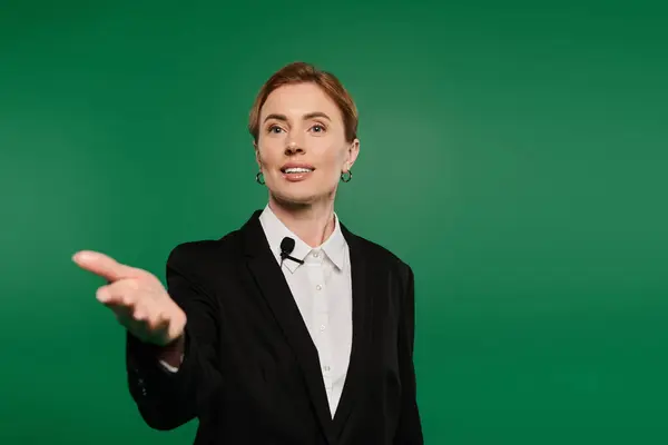 A poised television presenter in formal black attire captivates the audience against a vibrant green background. — Stock Photo