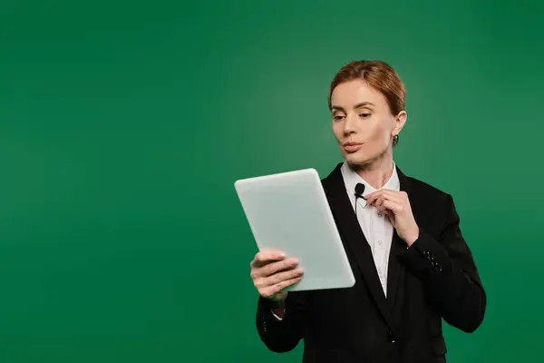The presenter in elegant black formal attire interacts with viewers while holding a tablet, showcasing charisma. — Stock Photo