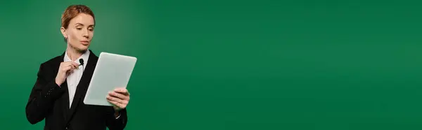 A poised TV presenter in stylish black formal wear interacts with audience on a vivid green background. — Stock Photo