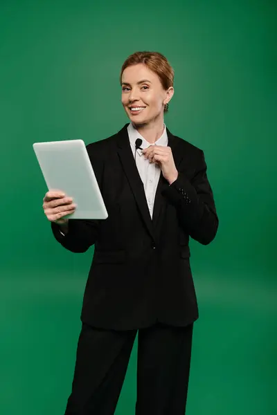 A confident TV presenter in sleek black formal attire interacts with an audience, holding a tablet. — Stock Photo