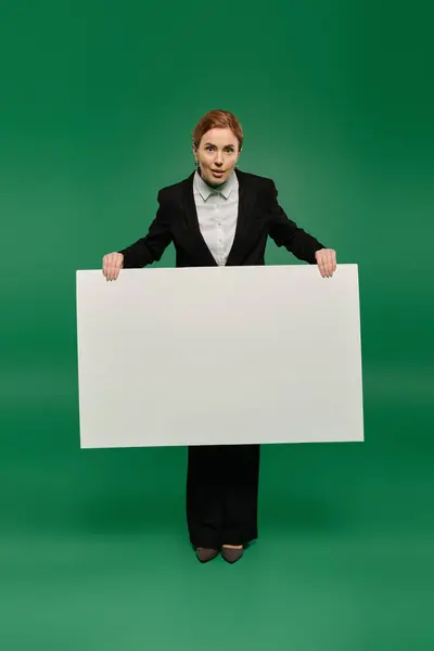 A skilled TV presenter in formal black clothing holding placard against a striking green background. — Stock Photo
