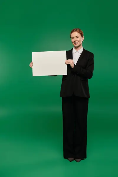 A TV presenter showcasing a blank sign in a formal black outfit, set against a lively green background. — Stock Photo