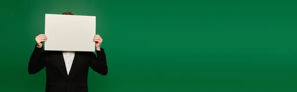 A stunning presenter dressed in formal black holds a blank sign while standing in front of a vivid green background. — Stock Photo