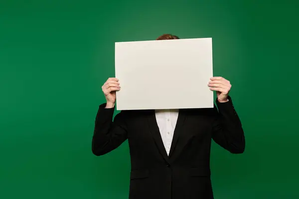 A TV presenter in black formal wear holds a blank sign in front of a bright green background. — Stock Photo