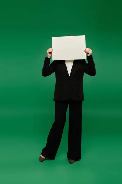 A stylish TV presenter in formal black clothing showcases a blank sign while standing in front of a green background. — Stock Photo