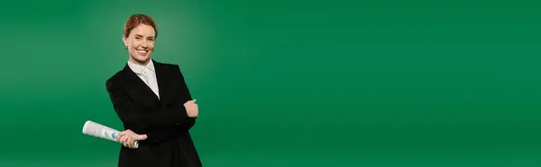 A poised presenter wearing black formal attire stands against a vibrant green backdrop, ready for broadcasting. — Stock Photo