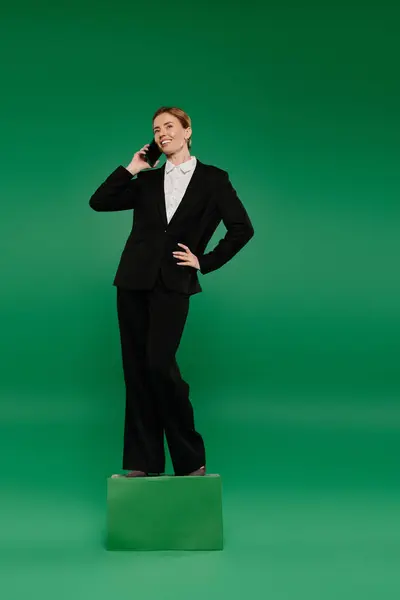 A confident TV presenter stands on a platform, discussing topics live with a phone against a bright green backdrop. — Stock Photo