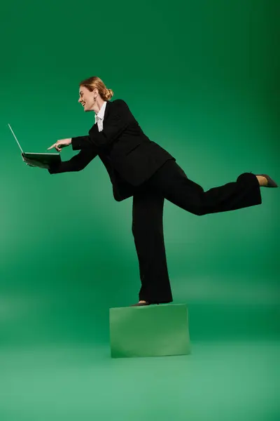 The talented presenter balances elegantly while holding laptop, exuding confidence in elegant black. — Stock Photo