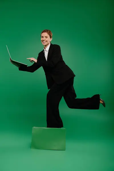 A cheerful TV presenter in black formal attire energetically interacts while standing against a green backdrop. — Stock Photo