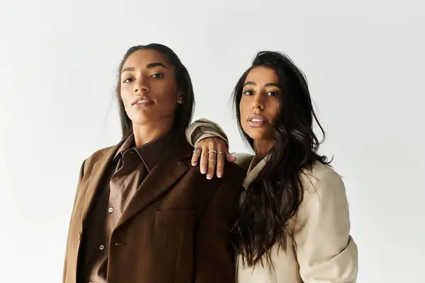 Dos mujeres jóvenes en trajes elegantes posan con confianza contra un telón de fondo minimalista. - foto de stock