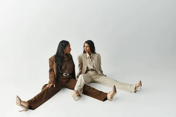 Duas jovens mulheres na moda vestidas com ternos chiques se envolvem em uma conversa cativante. — Fotografia de Stock