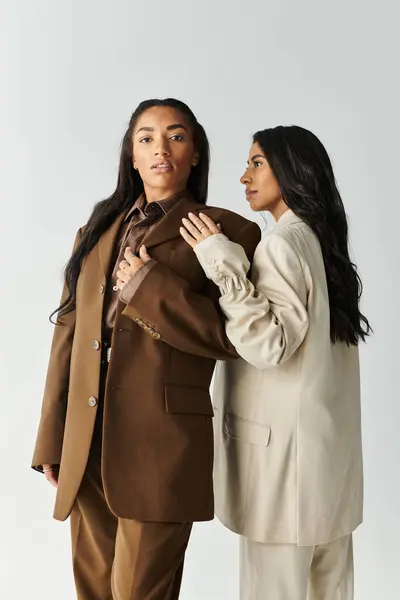 Two young women exude confidence in elegant, modern outfits, posing in a neutral toned studio. — Stock Photo