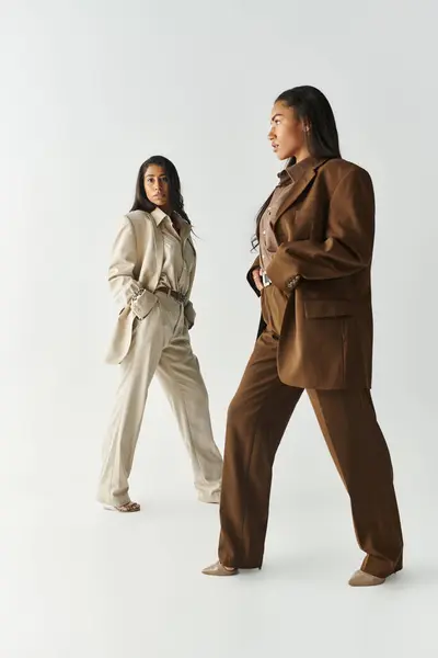 Two young women exhibit trendy fashion choices in a minimalist studio, radiating confidence. — Stock Photo