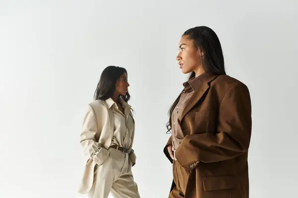 Two young and fashionable women pose confidently in stylish attire against a simple backdrop. — Stock Photo