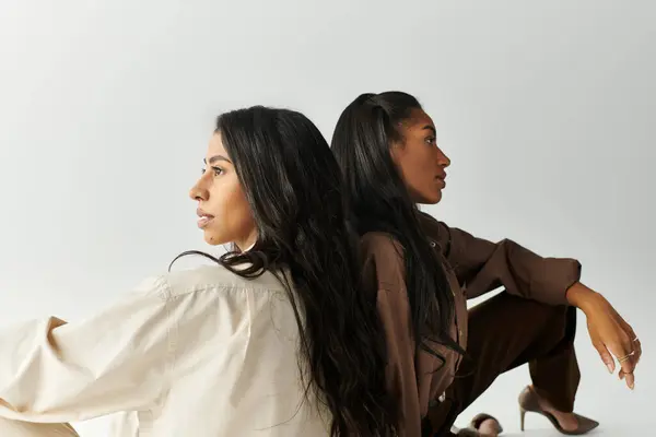 Two young women showcase their fashionable styles while posing creatively back to back. — Stock Photo