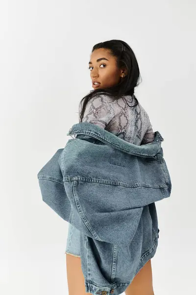 A young woman showcases her trendy outfit against a clean backdrop, exuding modern style. — Stock Photo