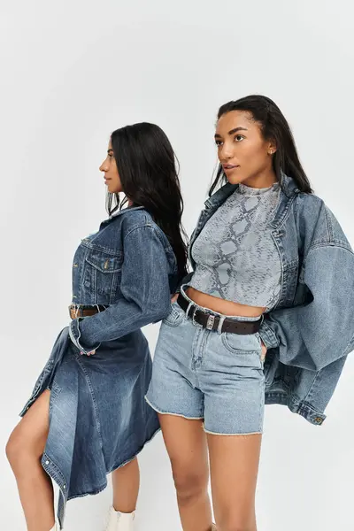 Two young women in fashionable denim outfits squat side by side, exuding trendy confidence. — Stock Photo