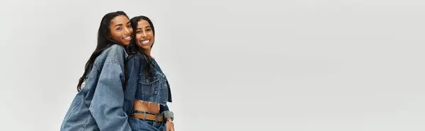 Two fashionable young women pose together in stylish denim outfits, radiating joy. — Stock Photo