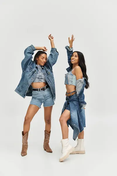 Two fashionable young women express joy while modeling chic denim ensembles in bright light. — Stock Photo