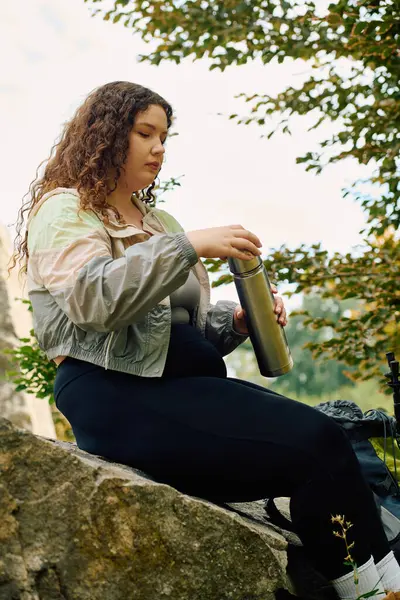 Красивая женщина plus size отдыхает в пышном лесу, выплескивая из термоса, пока пила природу. — стоковое фото
