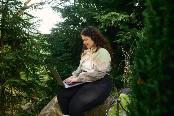 Una mujer de talla grande está profundamente comprometida con su computadora portátil en medio de la serena belleza de la naturaleza. - foto de stock