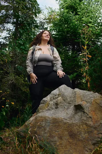 A radiant woman enjoys the beauty of nature, perched confidently on a large rock amidst greenery. — Stock Photo