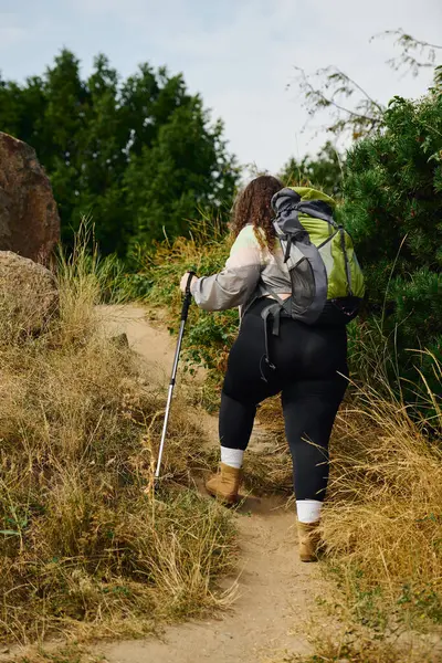 In a sunlit field, a plus size woman walks along a winding trail adorned with nature beauty. — Stock Photo
