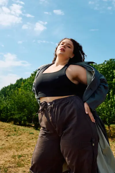 Una donna radiosa plus size si erge con fiducia in mezzo al verde lussureggiante, abbracciando la bellezza della natura. — Foto stock