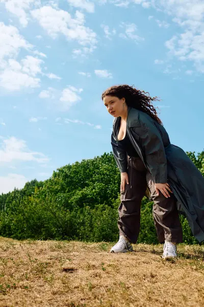 A joyful plus size woman bends down in a grassy field, embracing the beauty of nature around her. — Stock Photo