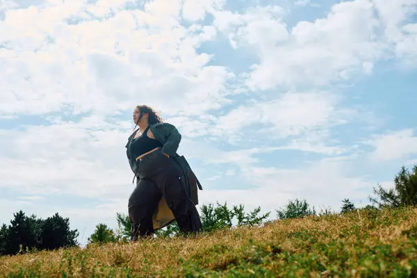 A beautiful plus size woman stands confidently amid the green field and blue sky. — Stock Photo