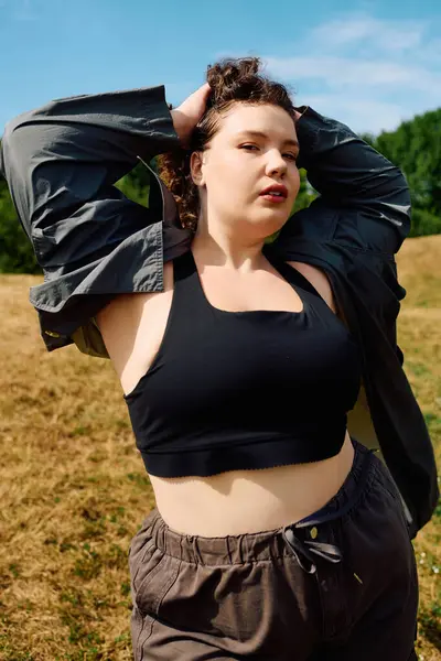 A plus size woman poses in a sunny field, confidently showcasing her style amidures beauty. — Stock Photo