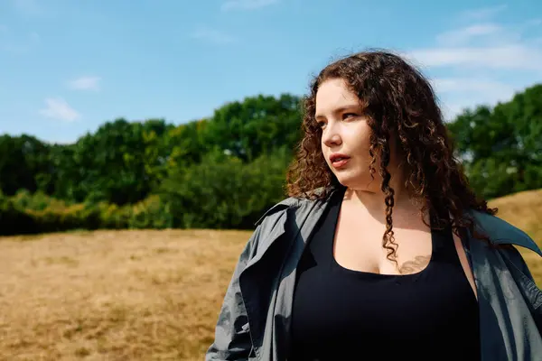 Eine selbstbewusste Plus-Size-Frau blickt nachdenklich in ein lebhaftes, sonniges Feld. — Stockfoto