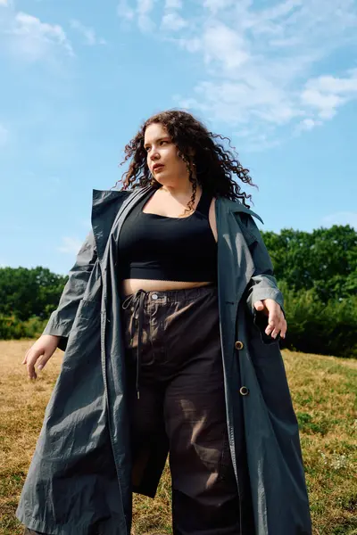 A confident woman embraces nature as she strolls through a sunlit field, showcasing her style. — Stock Photo