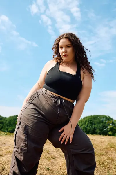 The beautiful woman poses confidently in a field under the bright blue sky. — Stock Photo