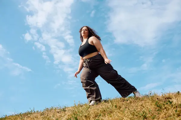 Uma bela mulher abraça a natureza enquanto caminha através de um campo verde exuberante sob um céu azul. — Stock Photo