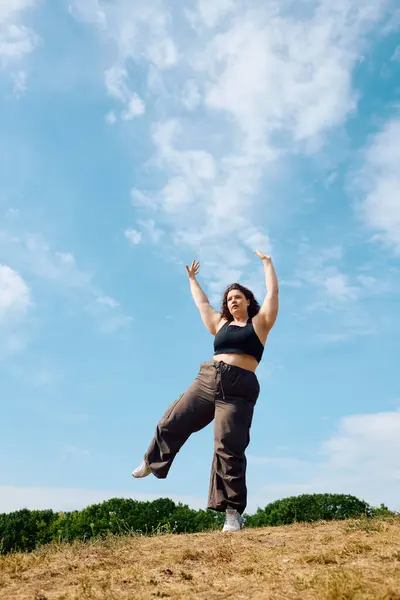 Une femme joyeuse de plus de taille danse librement dans un champ vibrant sous un ciel bleu vif. — Photo de stock