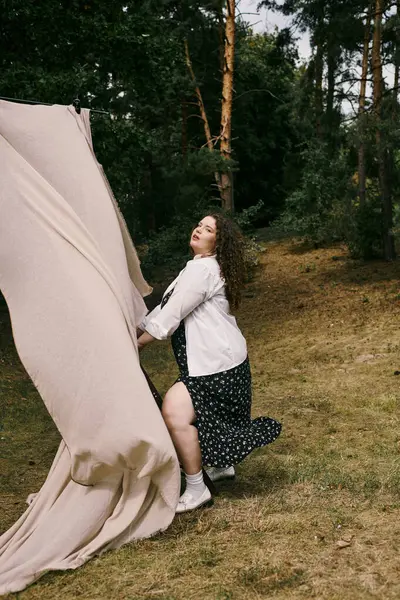 A beautiful plus size woman joyfully interacts with flowing fabric amidst a lush green field. — Stock Photo