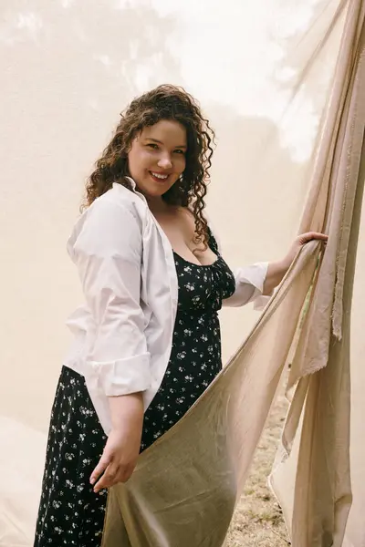 A beautiful plus size woman smiles warmly while holding a flowing fabric in a sunlit field. — Stock Photo