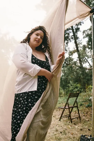 In a tranquil field, a beautiful plus size woman holds fabric, embodying confidence and grace. — Stock Photo