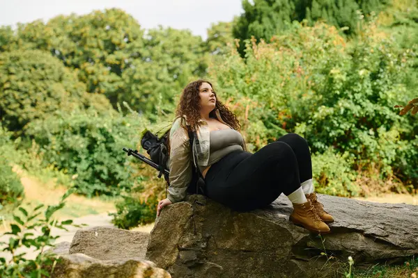 Красивая женщина plus size сидит на скале, впитывая окружающую ее атмосферу природы. — стоковое фото