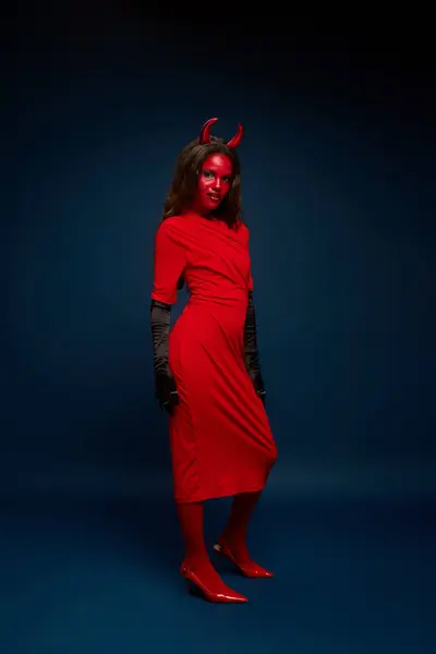 This beautiful woman showcases her creative Halloween costume, featuring red hues and devil horns. — Stock Photo