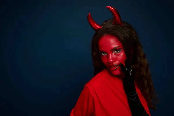 A stunning woman embodies the Halloween spirit with bold red makeup and playful devil horns. — Stock Photo