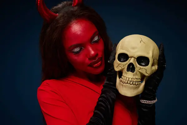 In a striking Halloween costume, a beautiful woman gazes at a skull, showcasing her artistic flair. — Stock Photo