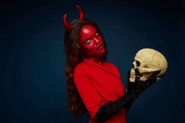 This enchanting woman, clad in a vibrant red outfit, channels Halloween vibes with a skull. — Stock Photo