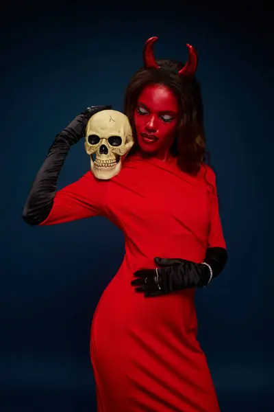 A captivating woman dressed in a haunting red outfit holds a skull, creating a spooky allure. — Stock Photo