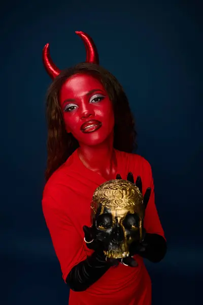 The striking woman in vibrant red makeup embodies a devilish character while holding a skull. — Stock Photo