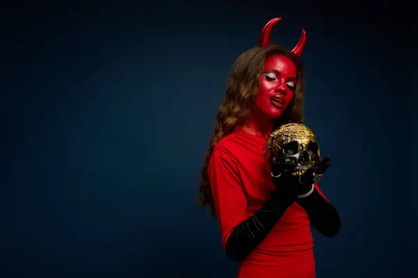 A stunning woman dressed as a devil embraces a decorative skull, exuding Halloween spirit. — Stock Photo