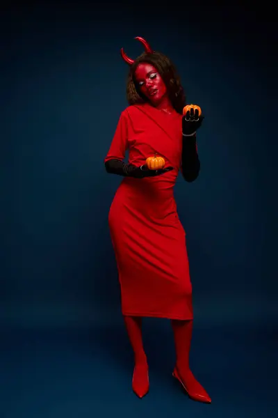 This woman embraces Halloween, wearing a bold costume and playfully interacting with pumpkins. — Stock Photo